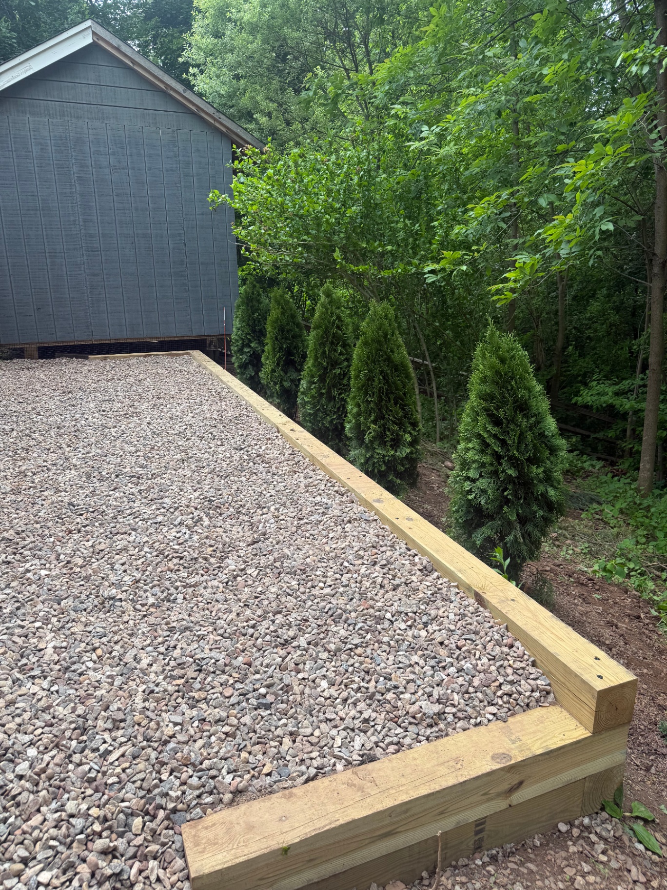 Gravel pad with timber border and arborvitae plantings